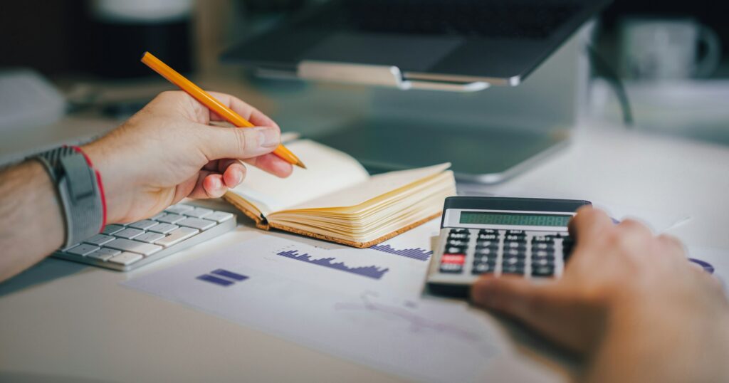محاسب يدوّن ملاحظات بجوار آلة حاسبة وتقارير مالية